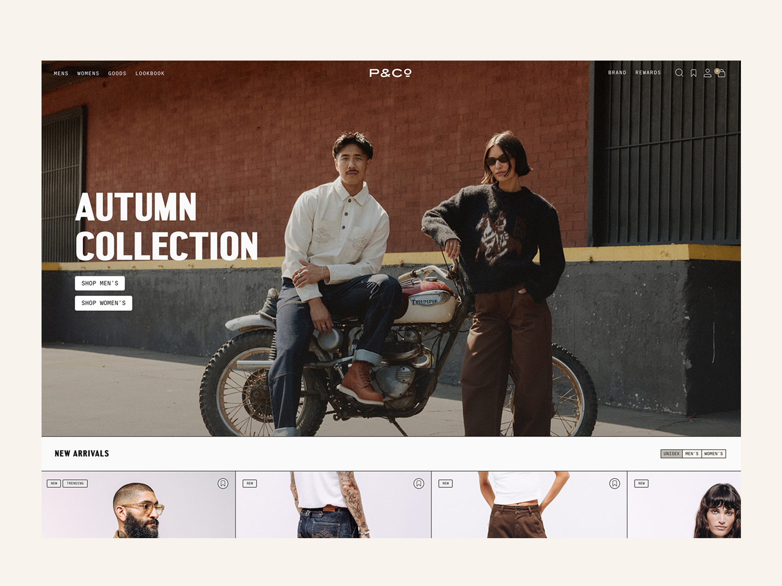 Man sitting on a vintage Triumph motorcycle wearing a white shirt and boots, and woman standing beside him in sunglasses, sweater, and brown pants, against a brick wall with Autumn Collection text.